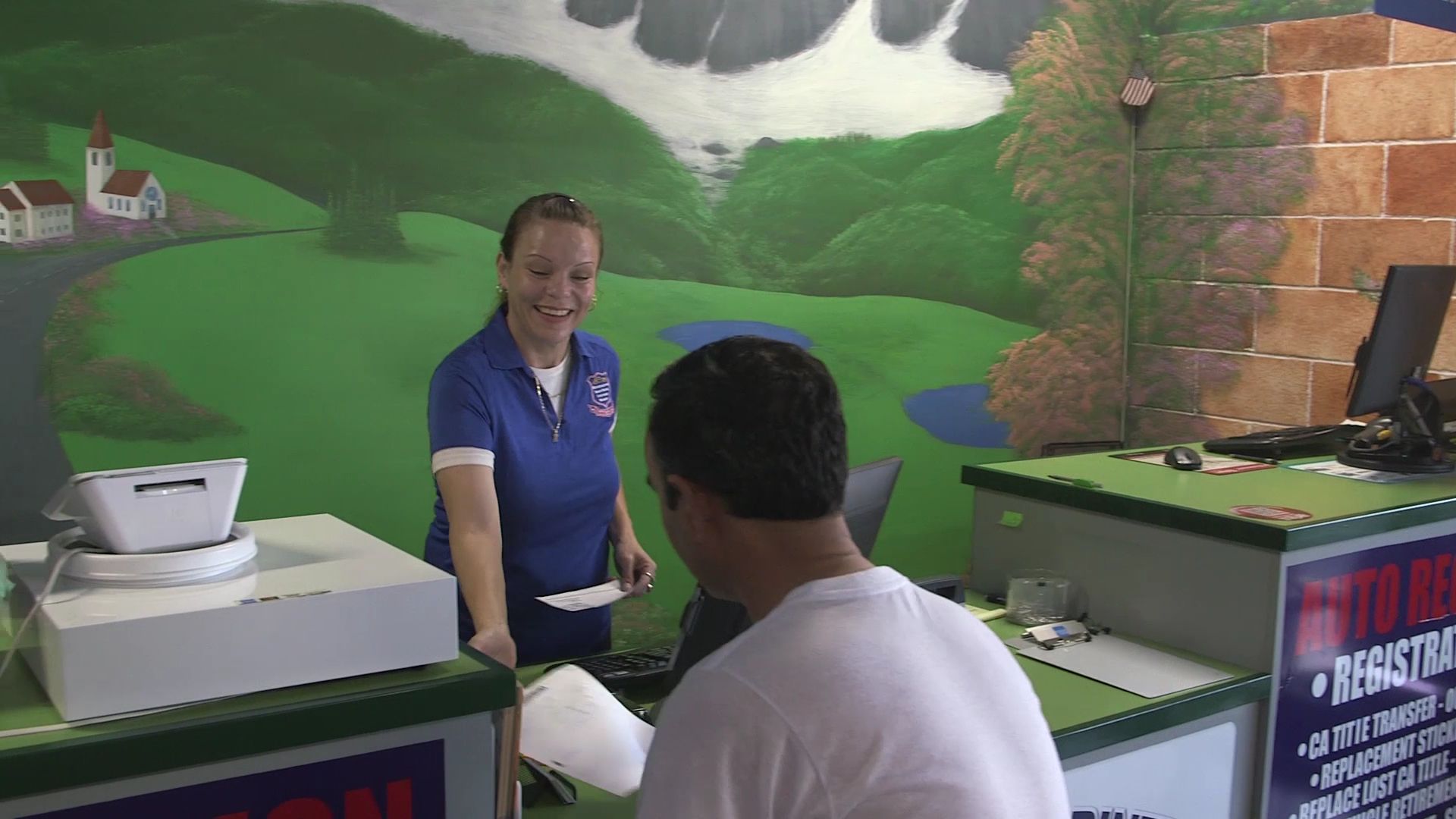Woman at a counter talking to a seated customer in a shop with green mural walls.