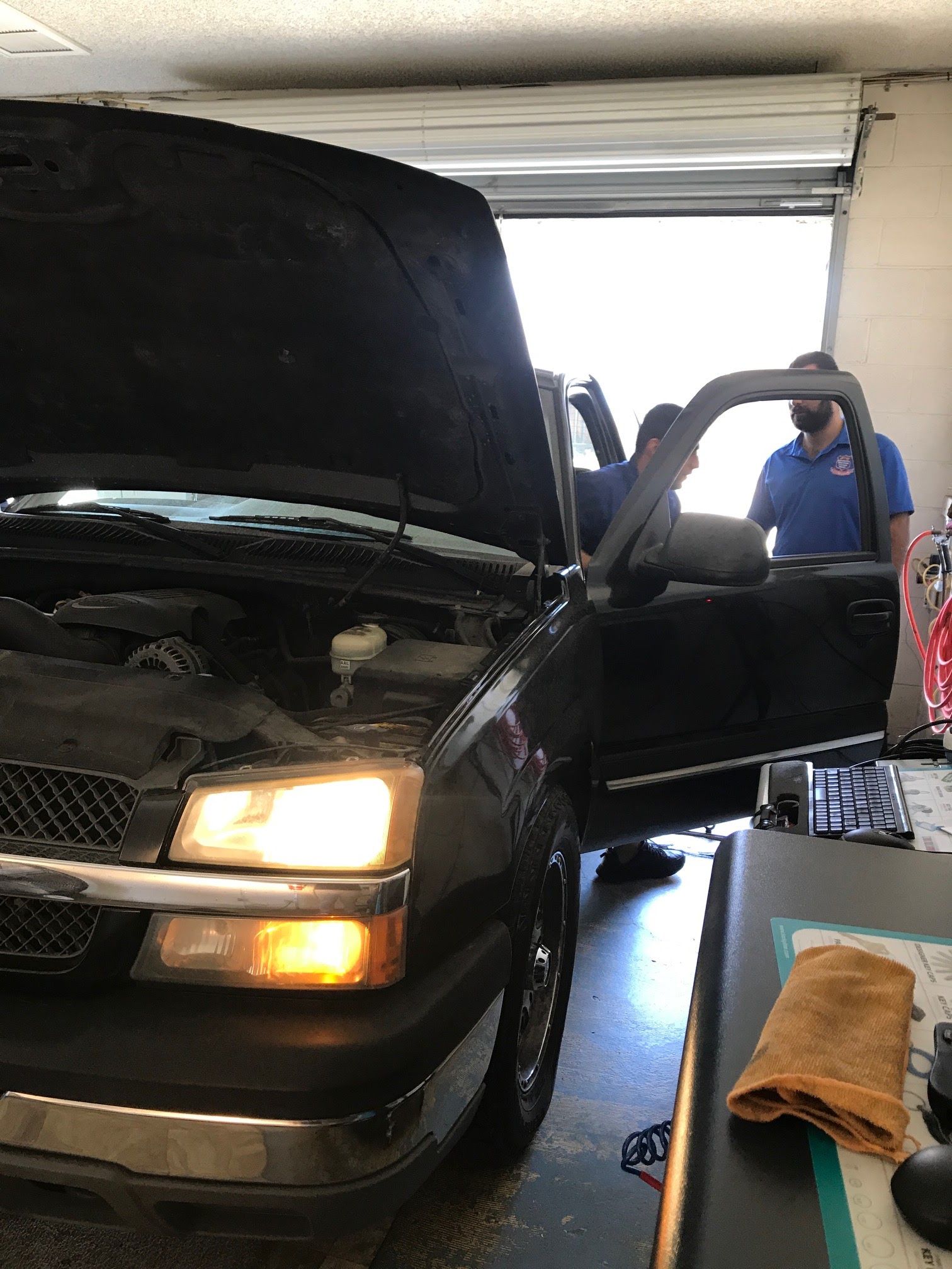 Black pickup truck with hood open in a garage, a person standing by the open door.
