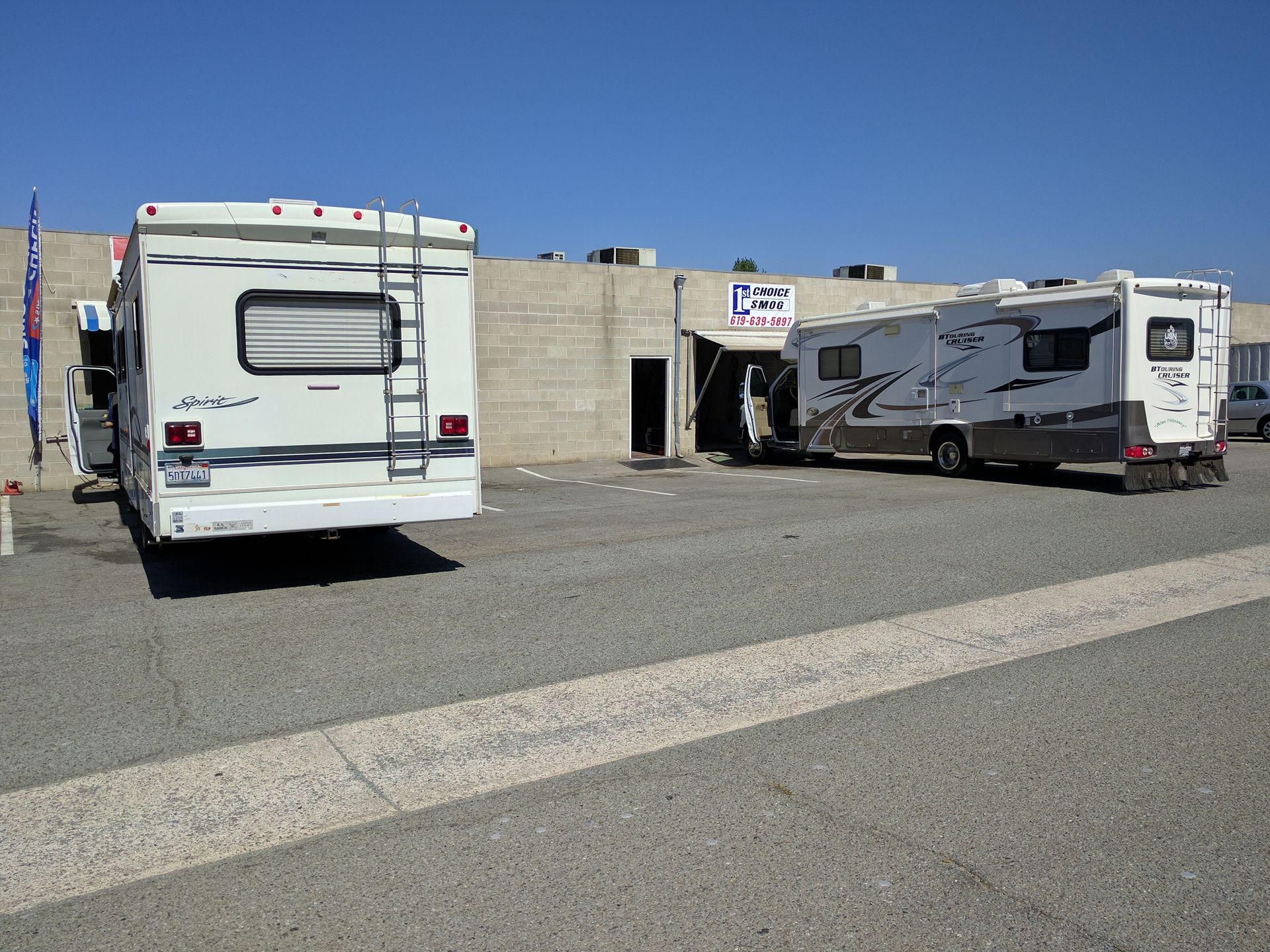 Two RVs parked on a gravel lot beside a concrete wall under a clear blue sky.