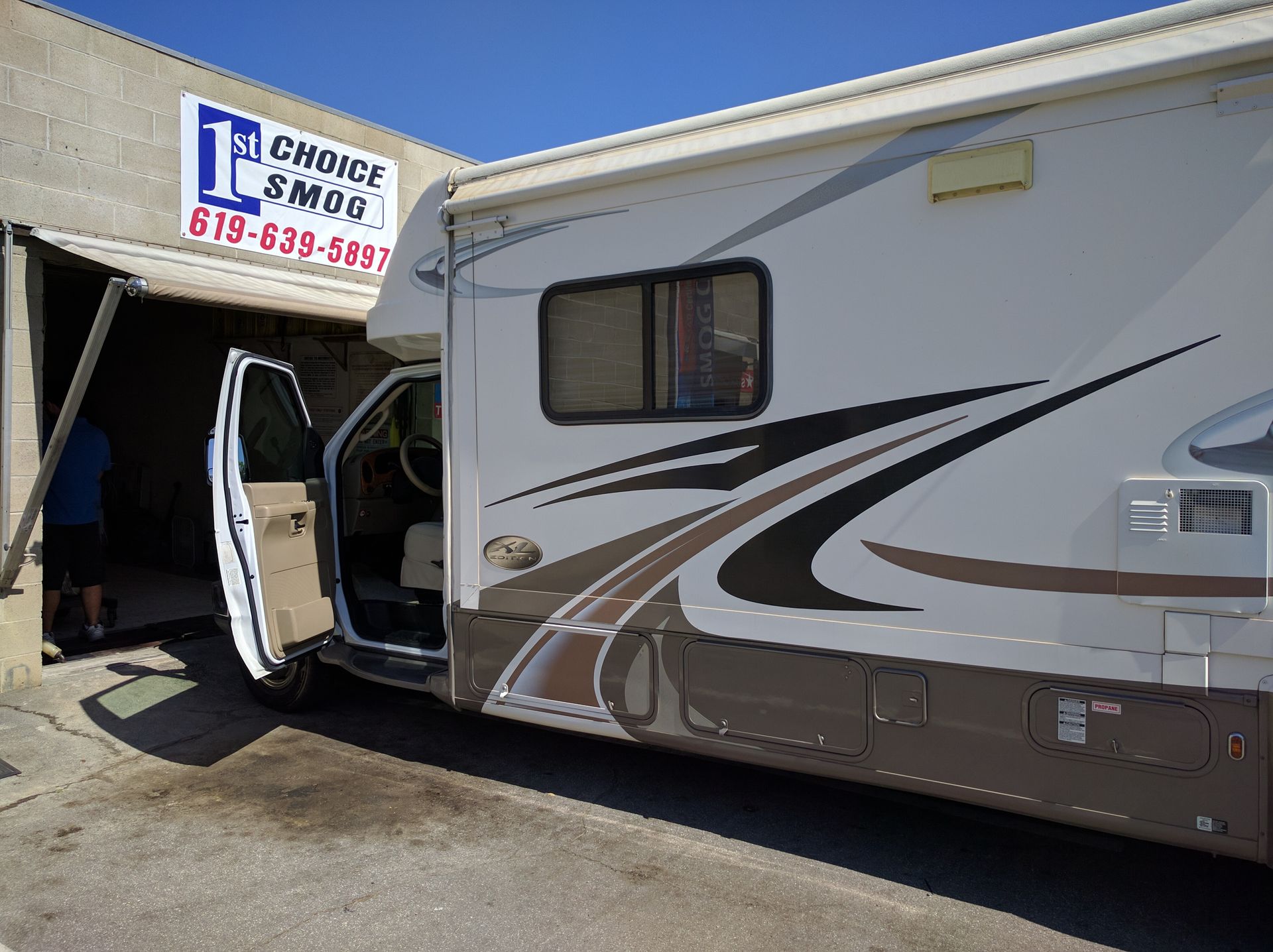 RV at a garage entrance with the side door open, showing a white and silver exterior under blue sky.