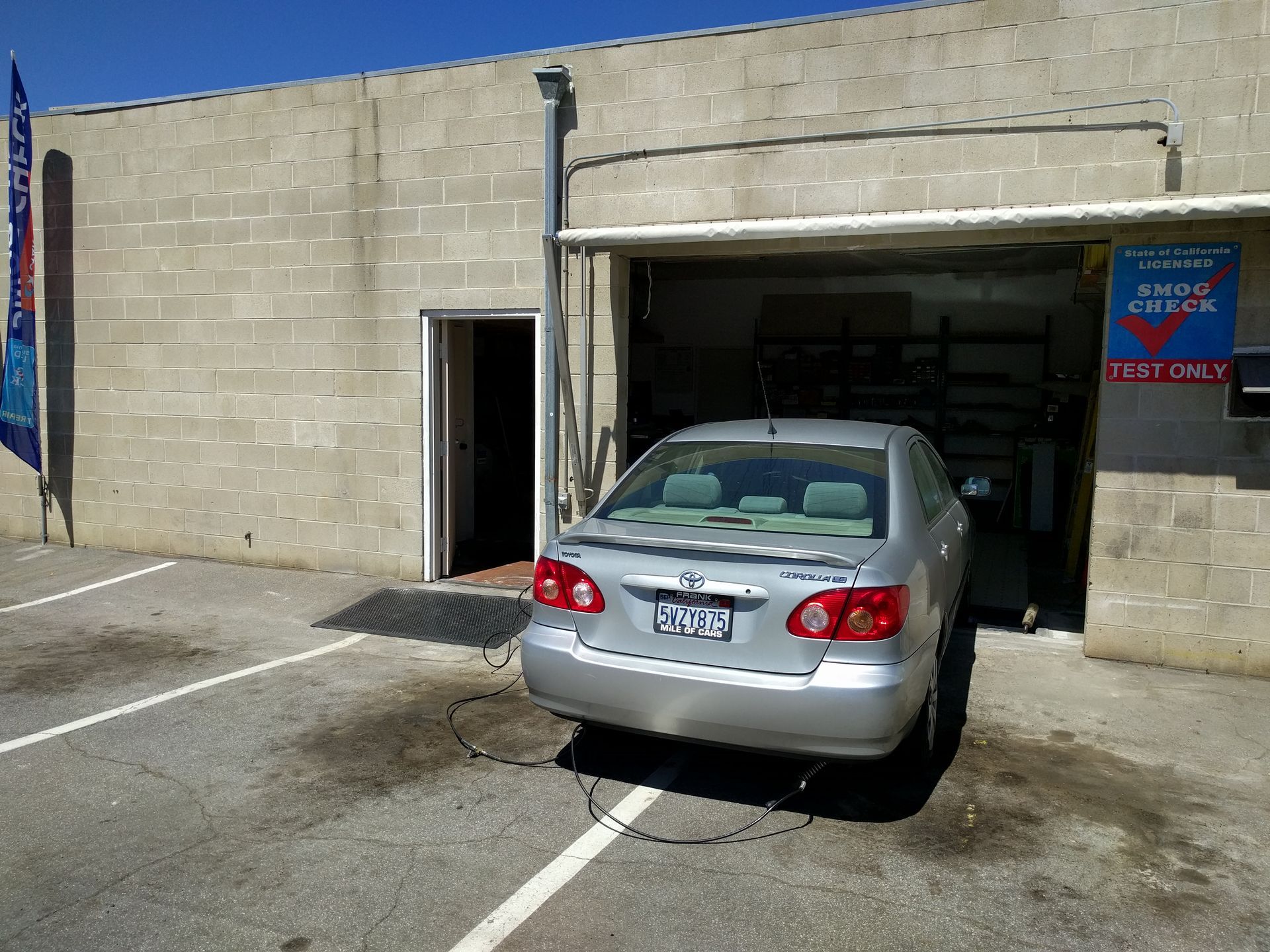 Silver sedan parked half in a garage of a tan cinderblock building