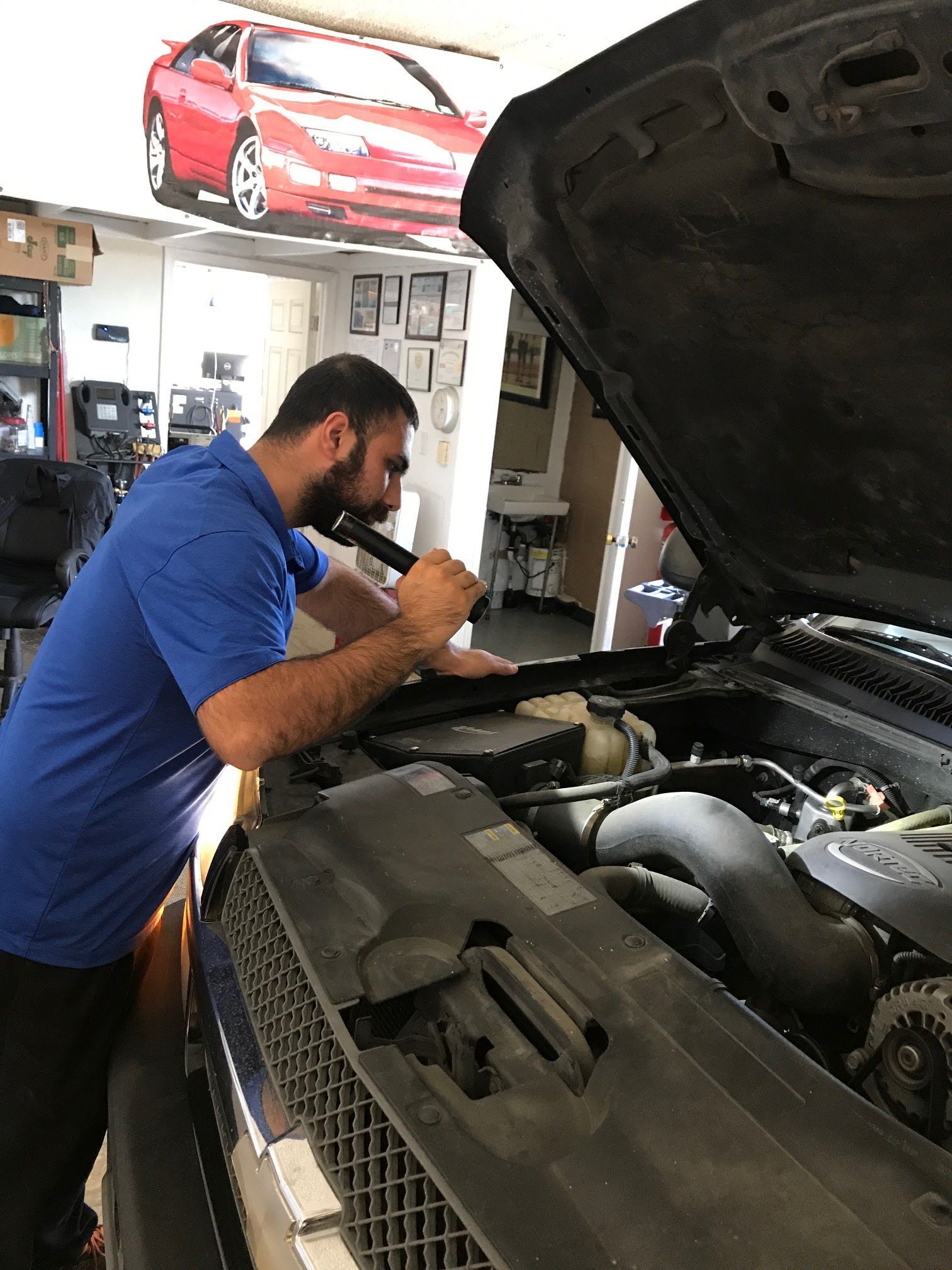 Mechanic in blue shirt inspecting a car engine with hood open in an auto shop