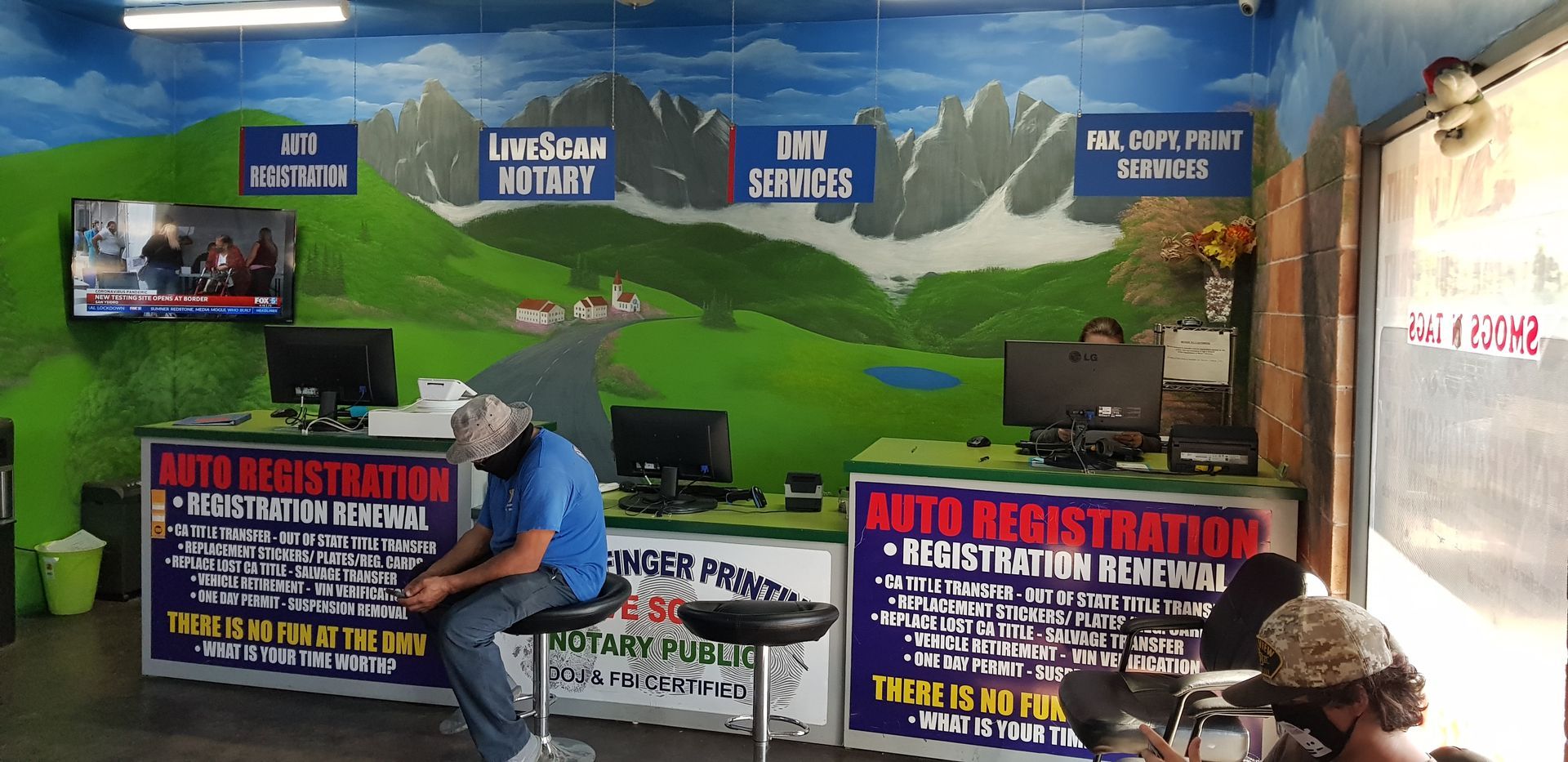 Indoor auto registration booth with signs, a seated person, and a mountain-themed wall mural