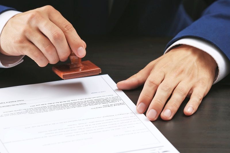 Hands stamping a document with a red seal on a desk