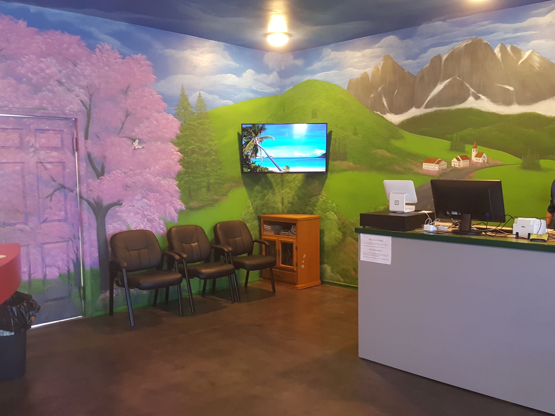 Reception area with mural of hills and cherry blossoms, chairs, wall TV, and a front desk.