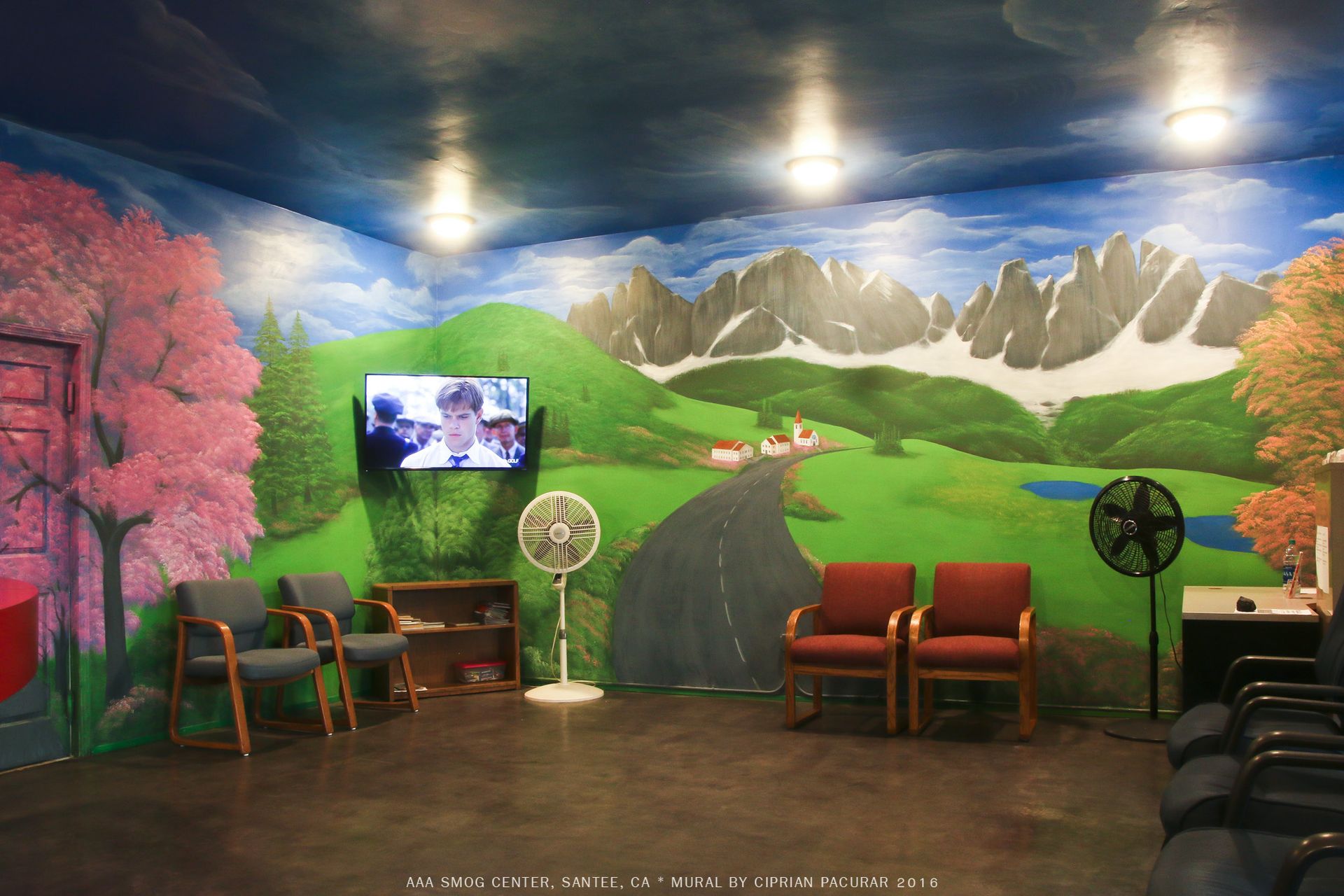 Mural-painted waiting area with chairs, fans, TV, and a winding path through green hills and mountains