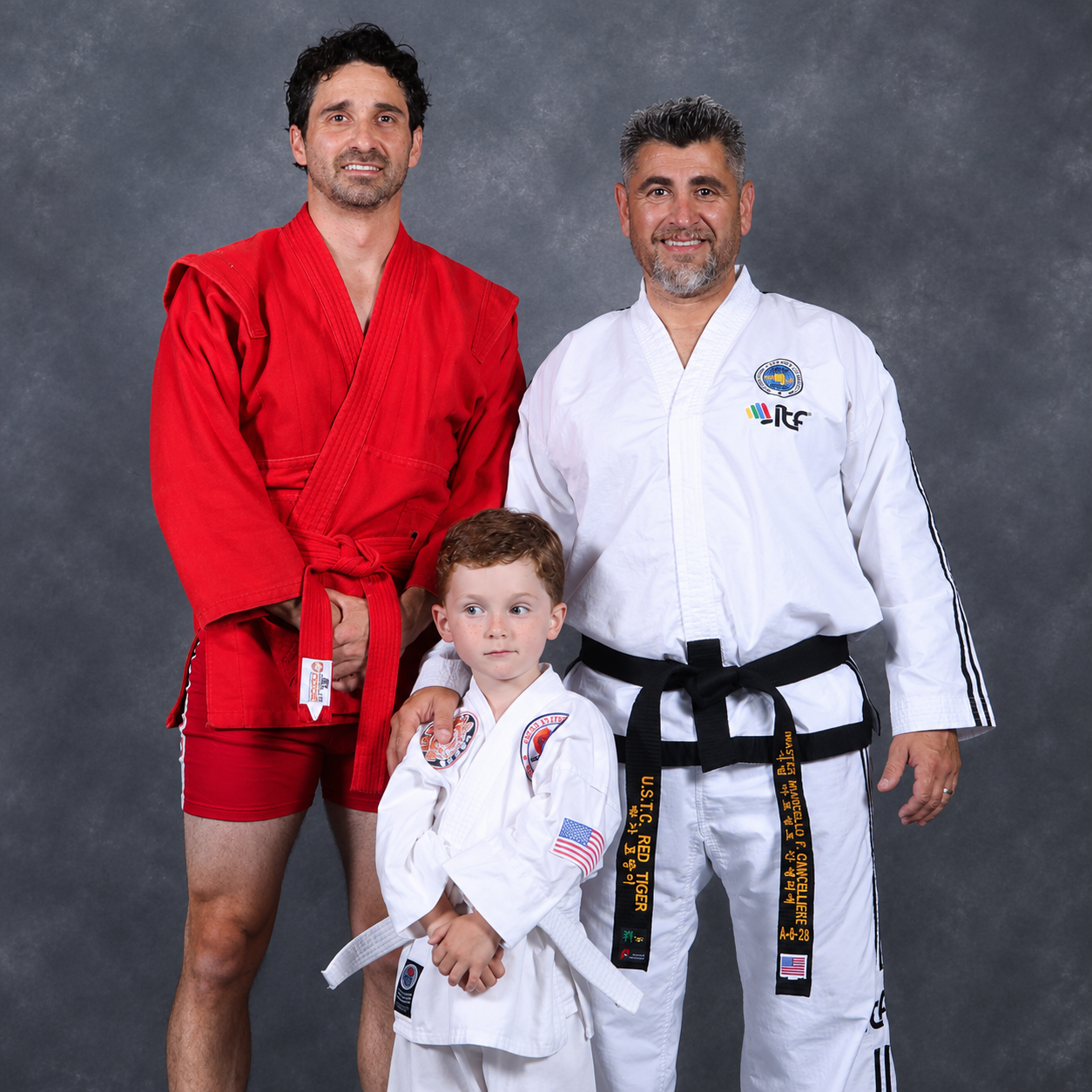 Three martial artists in red and white gis pose in a studio, one child centered in front.