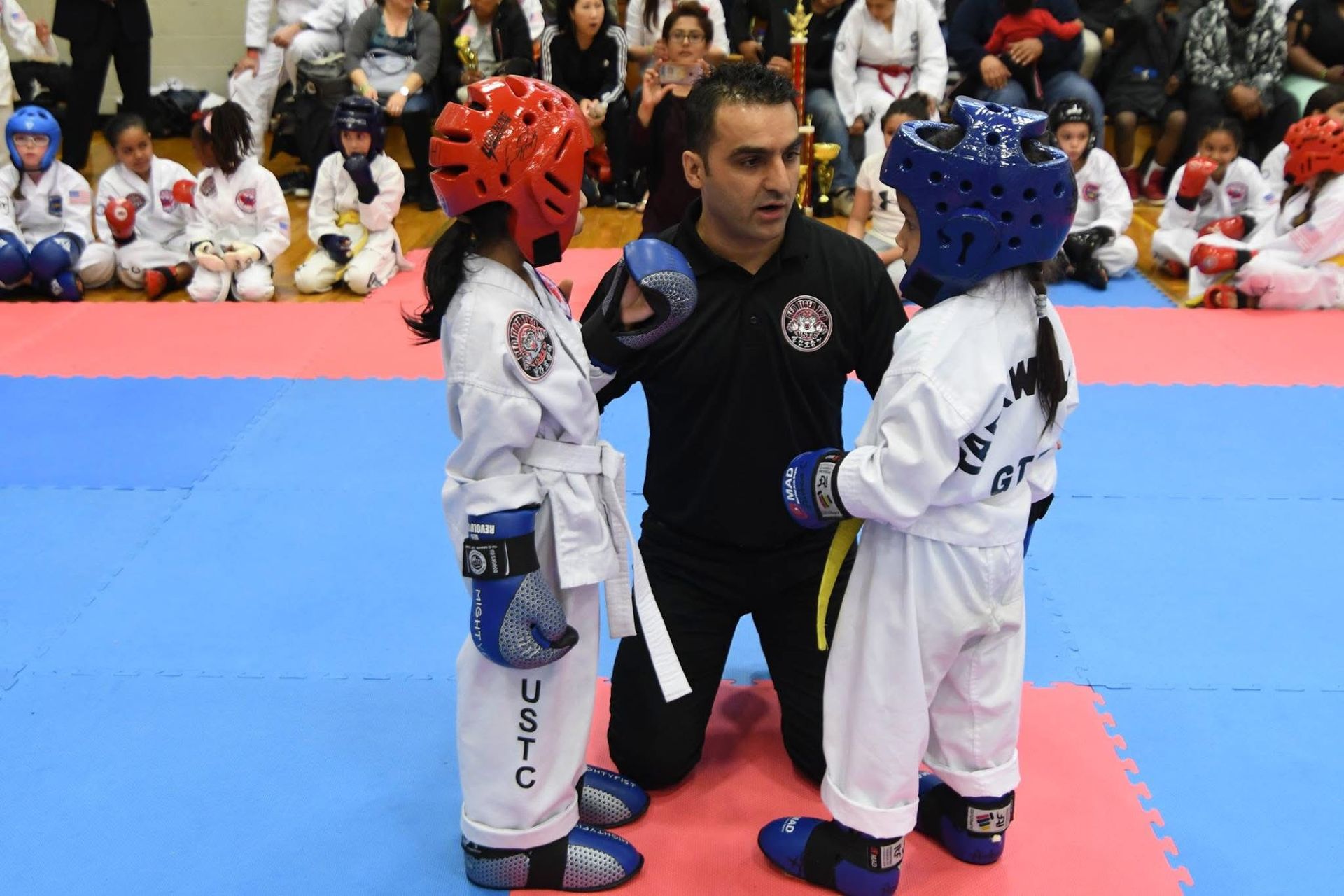 Three martial artists in red and white gis pose in a studio, one child centered in front.