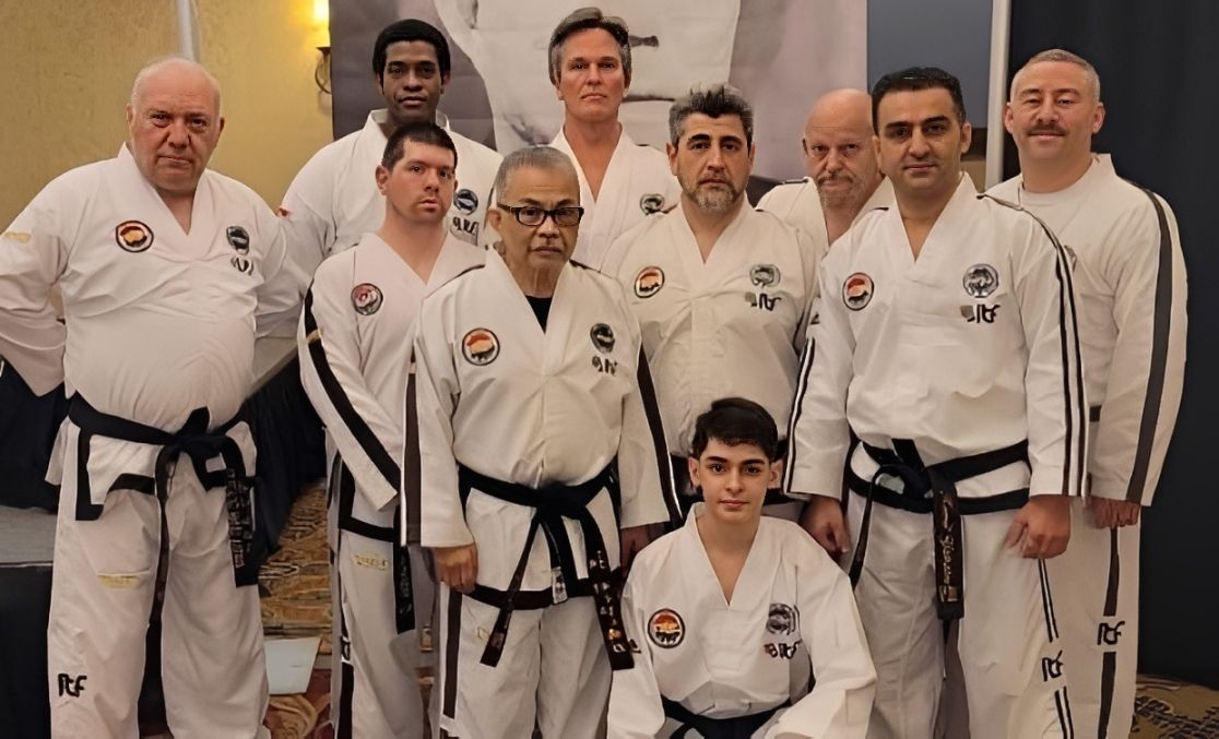 Martial arts class posing behind a star-spangled table with a celebratory cake and trophies