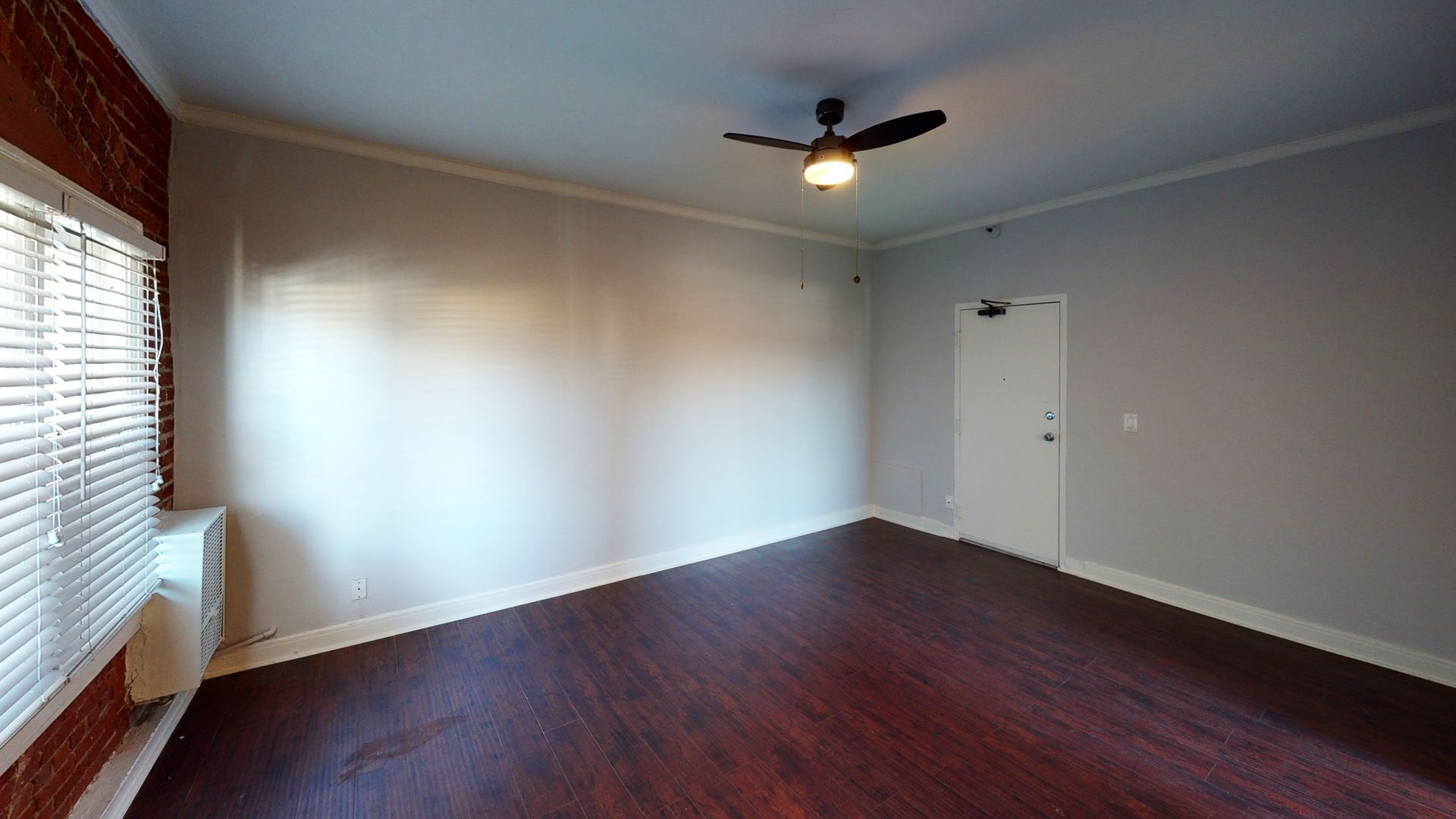 Empty room with dark wood floor, white walls, window with blinds, and ceiling fan.