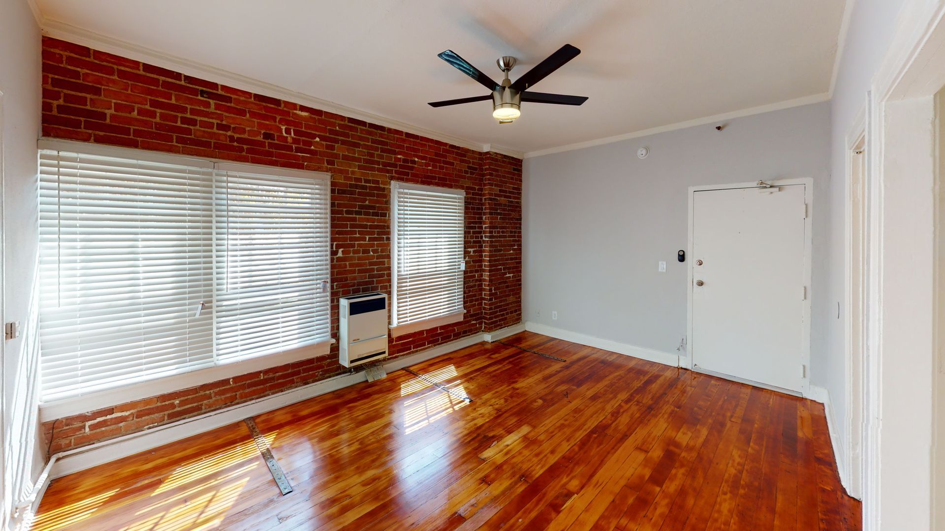 Living room with exposed brick wall, wood floors, and ceiling fan.