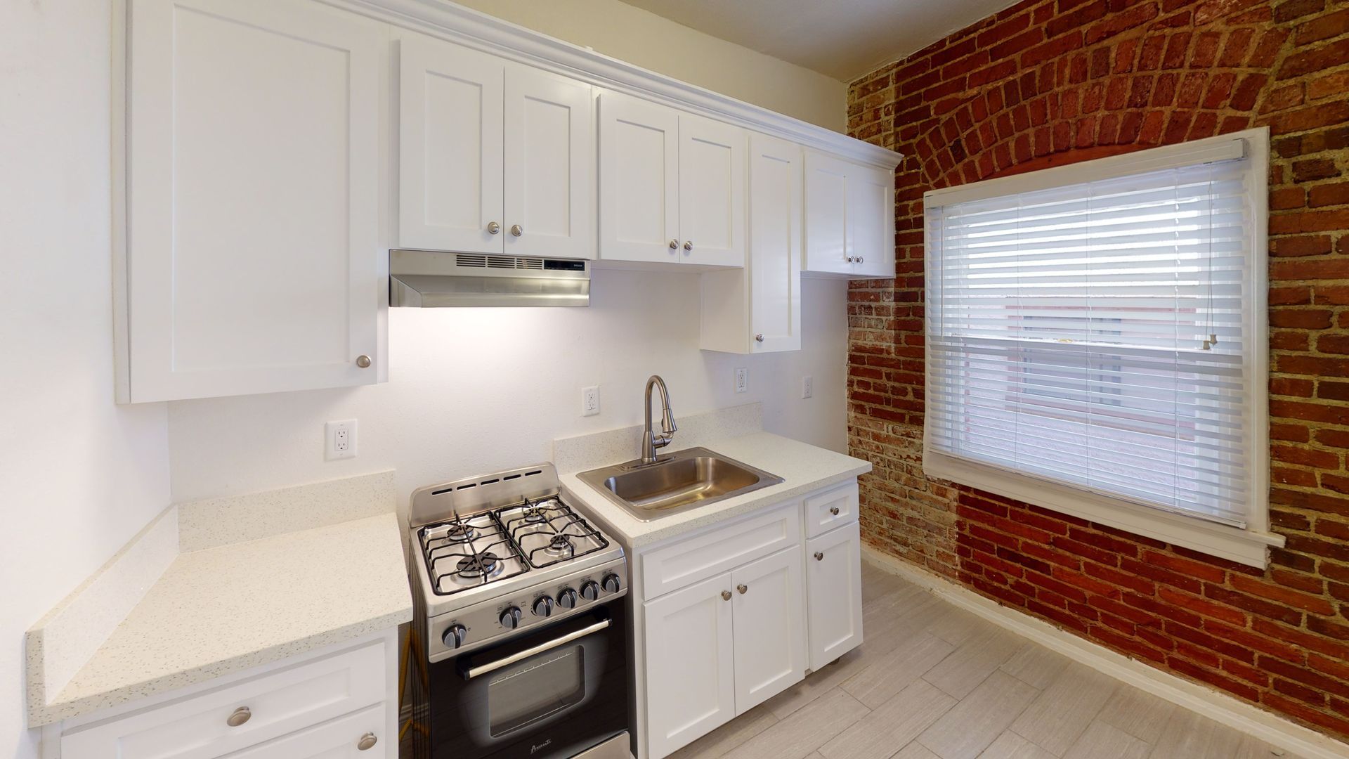Small kitchen with white cabinets, stove, sink, and exposed brick wall.