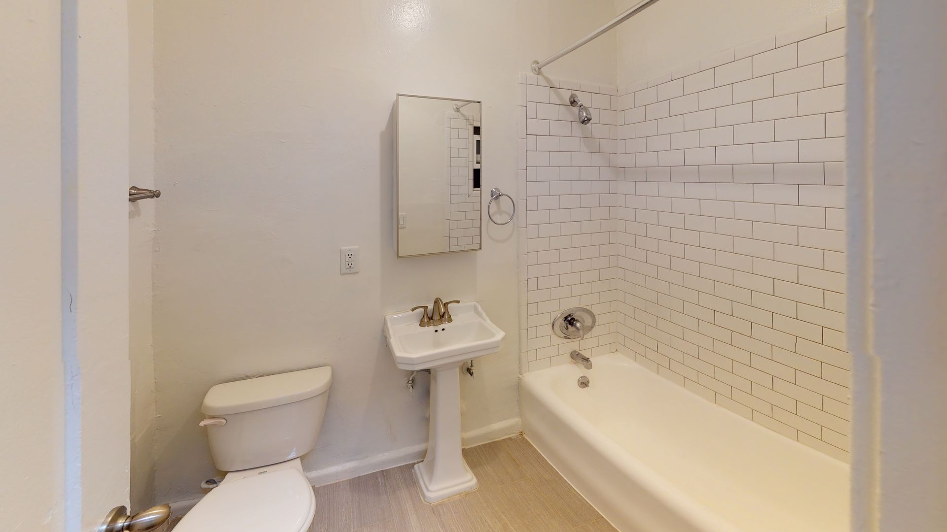 White bathroom with a toilet, pedestal sink, medicine cabinet, and a bathtub with a showerhead.