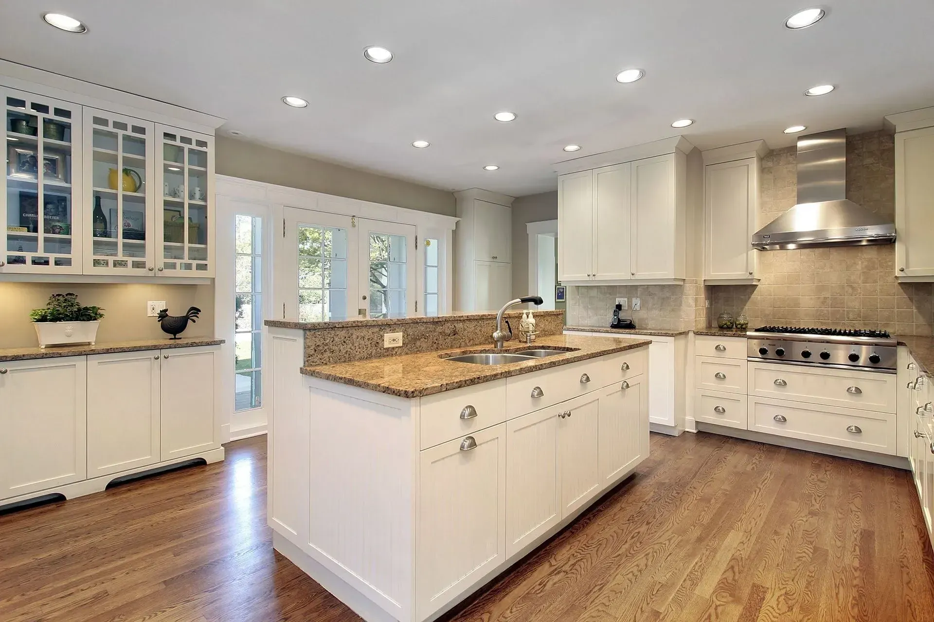 A kitchen with white cabinets , granite counter tops , stainless steel appliances and hardwood floors.