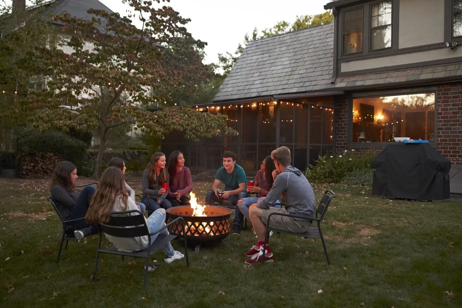 A group of people are sitting around a fire pit in a backyard.