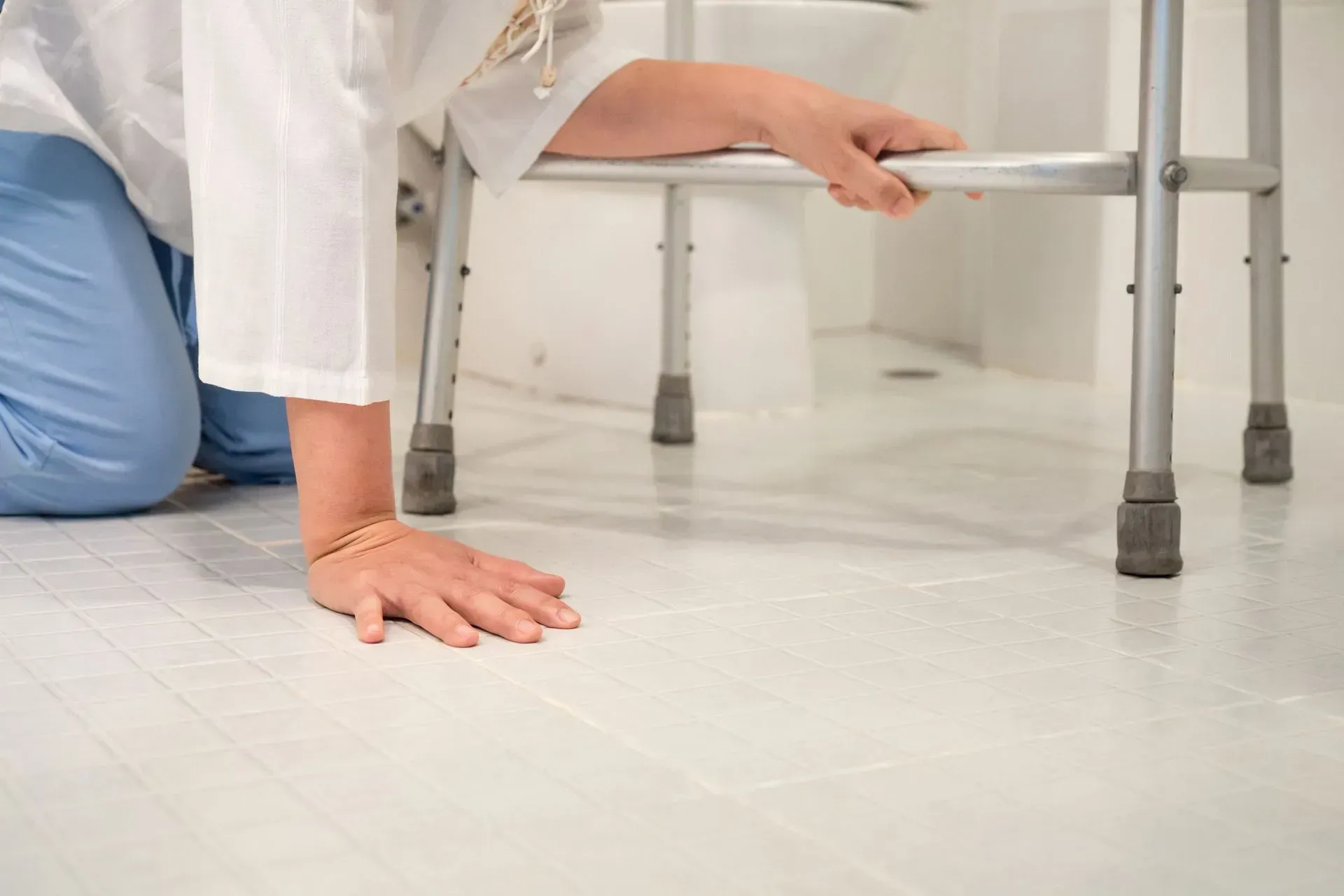A woman is kneeling on the floor next to a walker.