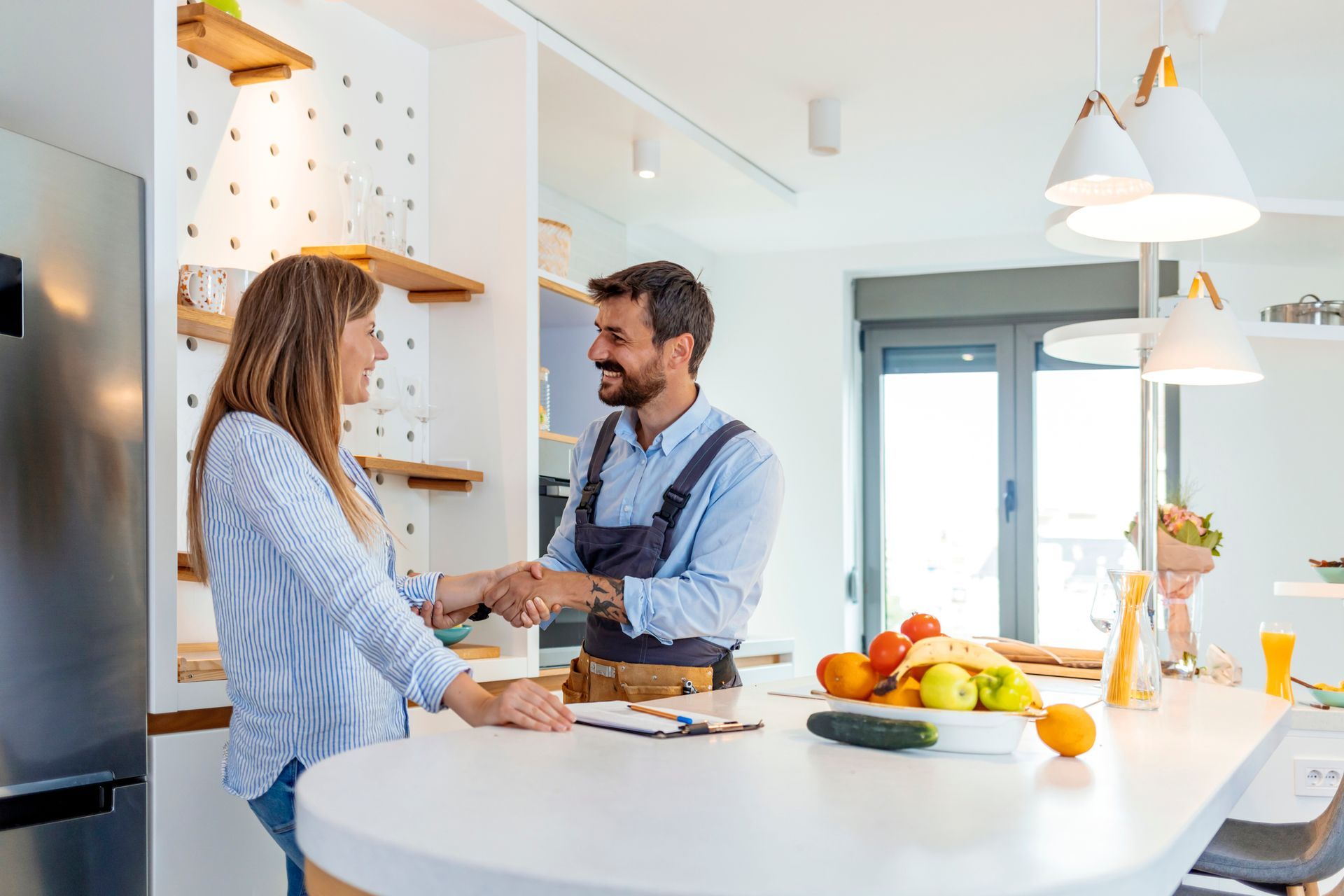 A smiling customer thanking a plumber with a handshake for his work in her kitchen. A smiling customer thanking a plumber with a handshake for his work in her kitchen.