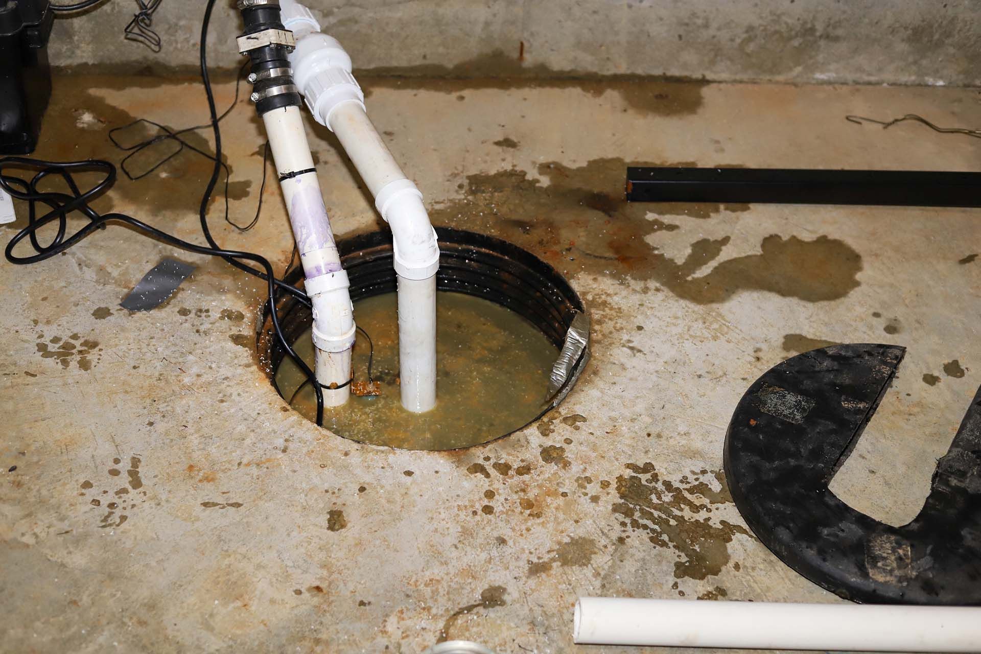 A drain hole in a basement with pipes coming out of it