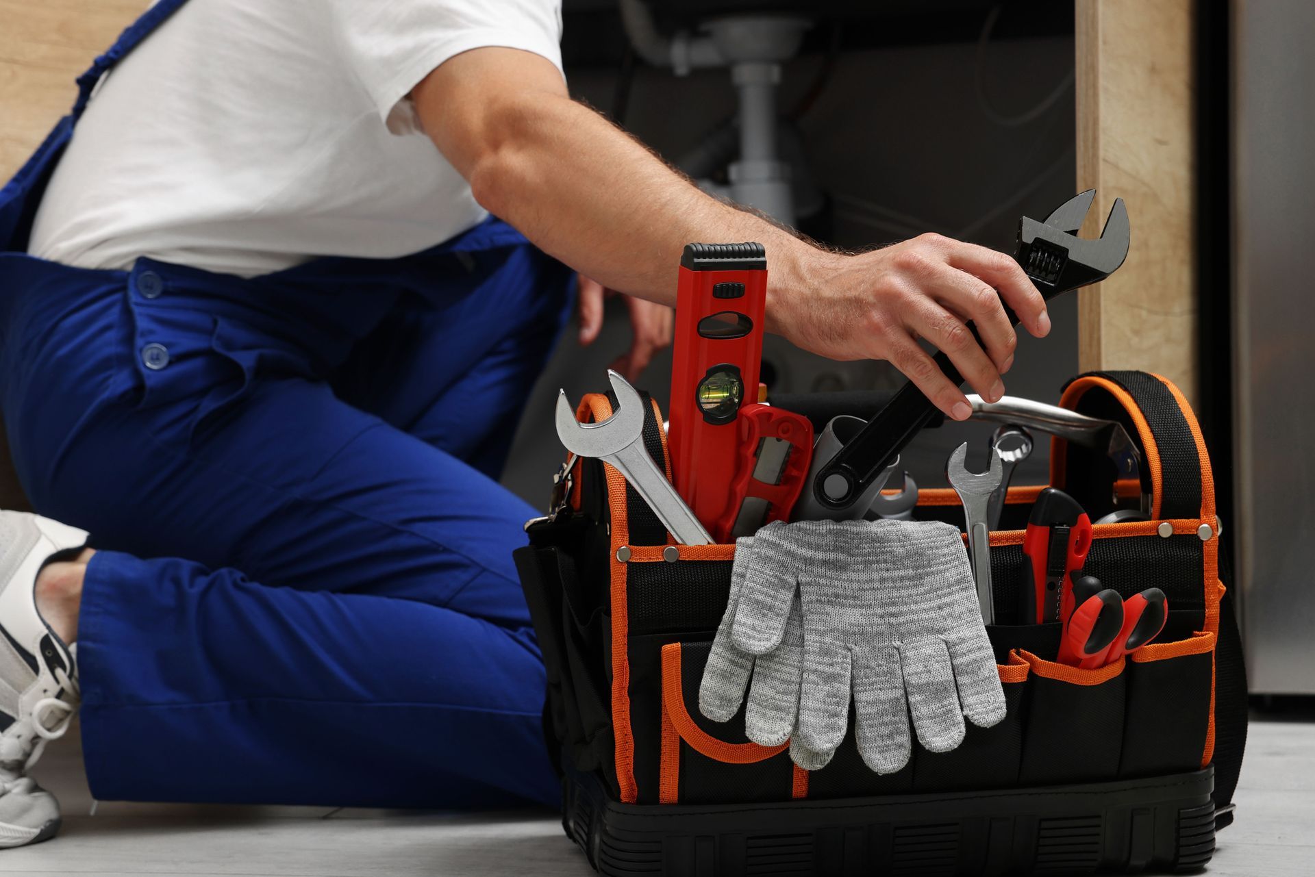 A plumber wearing a blue uniform, taking an adjustable wrench from a tool bag.