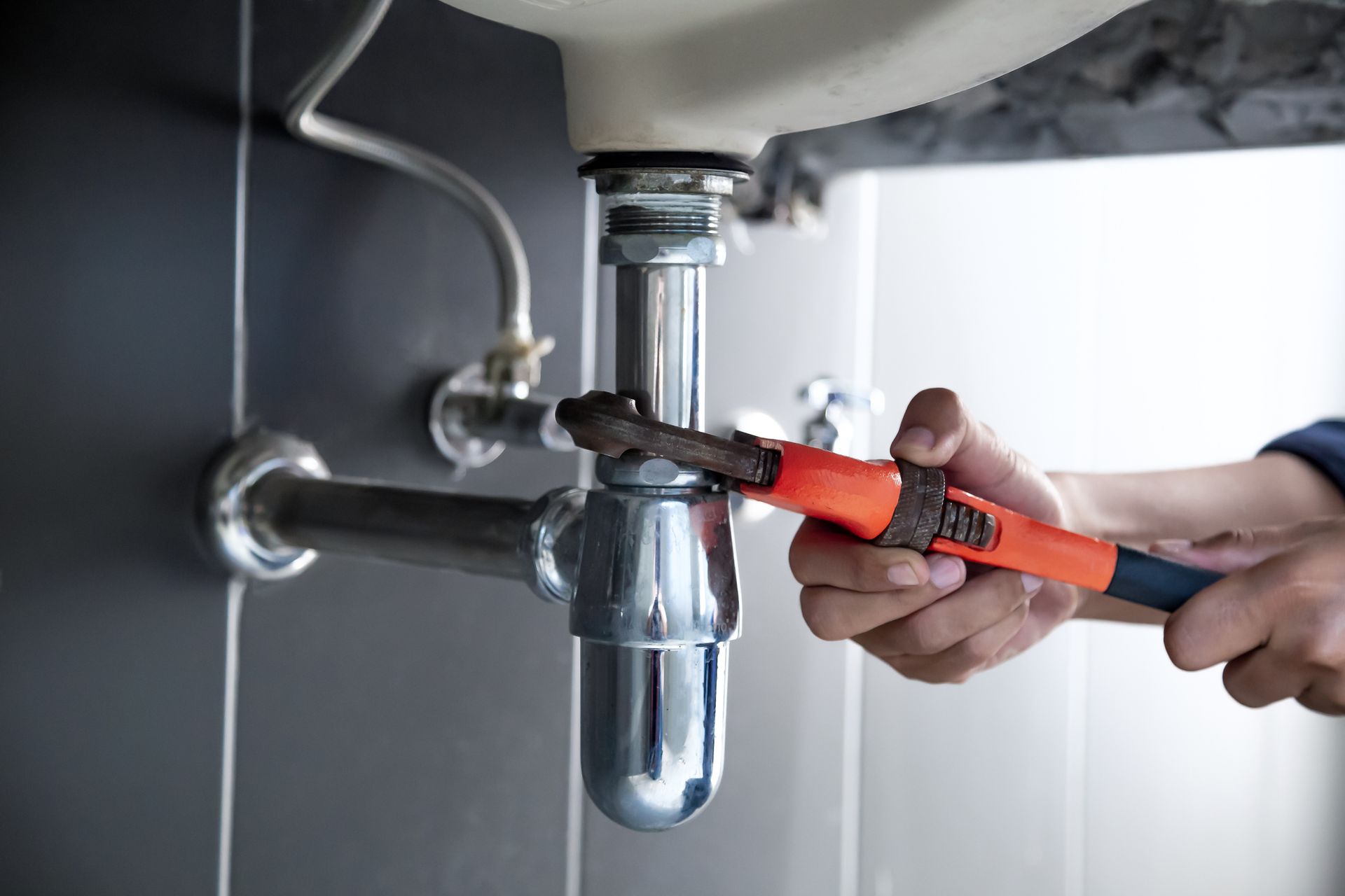 Plumber uses wrench to repair water pipe under sink | Oak Creek Plumbing & Remodeling | Milwaukee WI