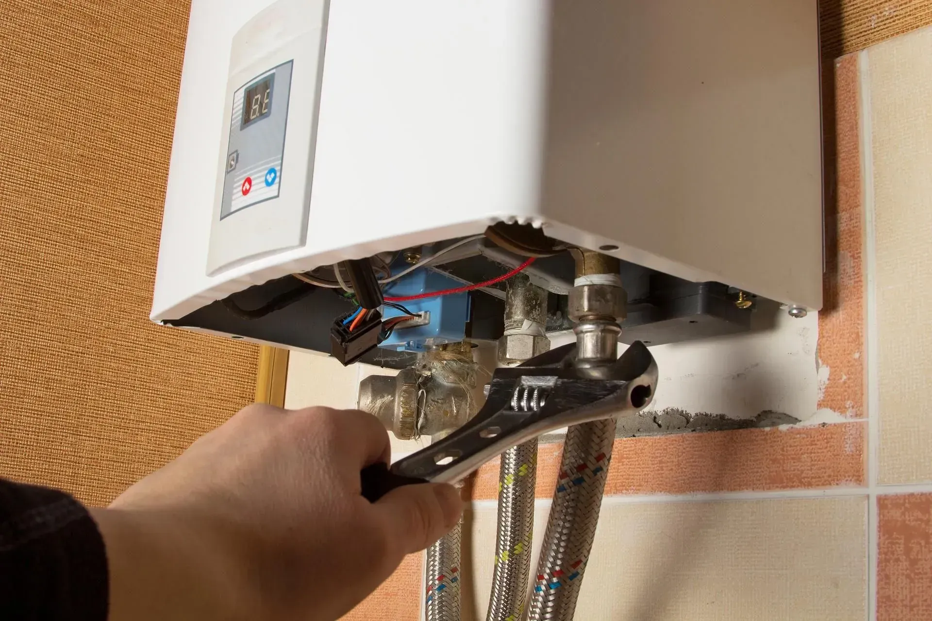 A person is fixing a water heater with a wrench.