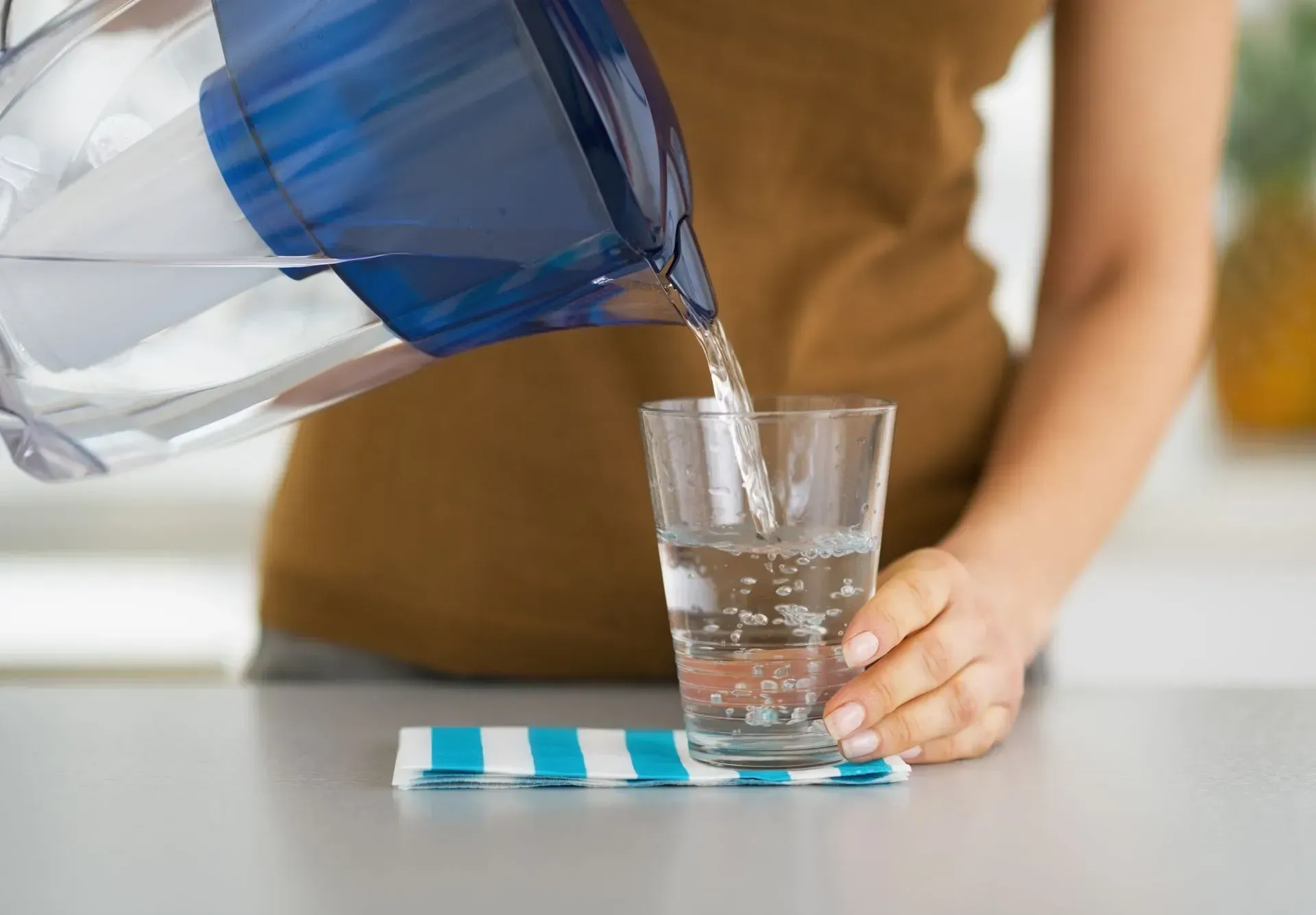 A woman is pouring water from a pitcher into a glass.