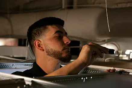 A man with a beard is working on a ceiling with a screwdriver.