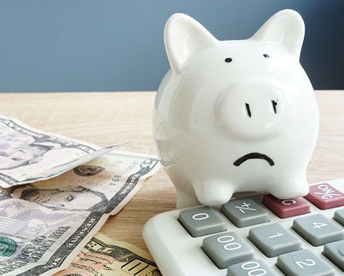 A piggy bank sitting on top of a calculator next to some money