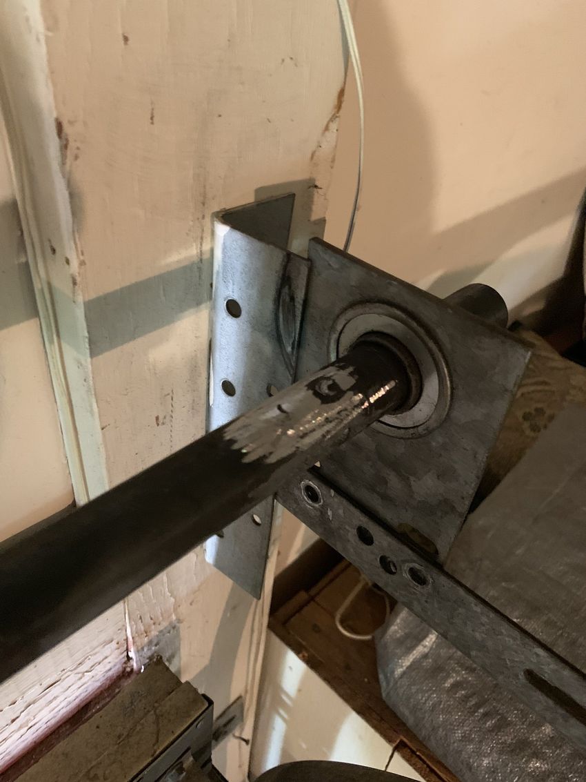 Close-up of a metal shaft passing through a mounted bearing bracket on a wooden wall.