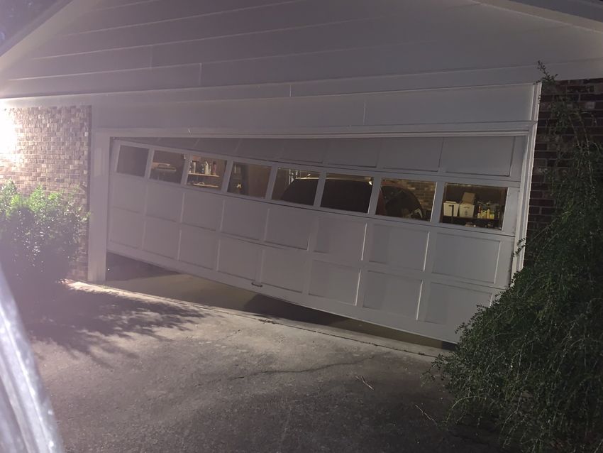 White garage door at night, lit by a porch light, with driveway and bushes beside it.