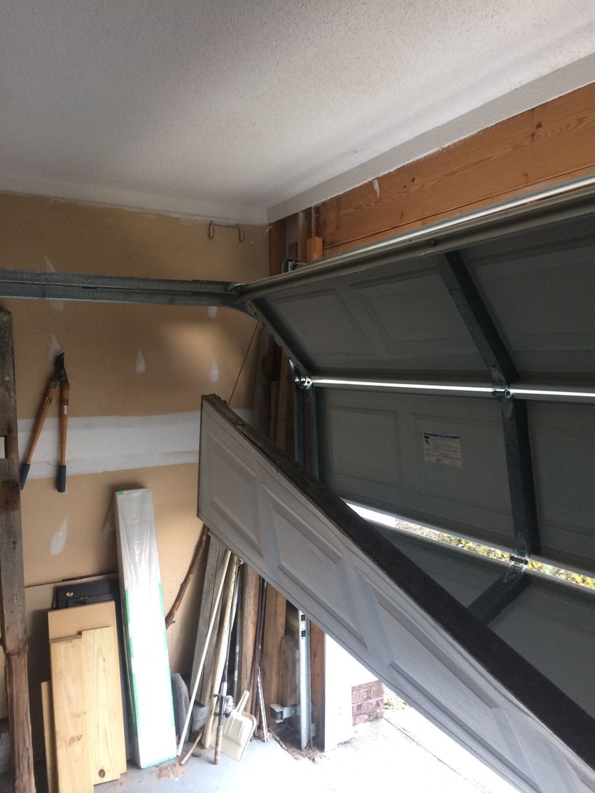 Open garage door with metal tracks and stacked boards along a tan wall.