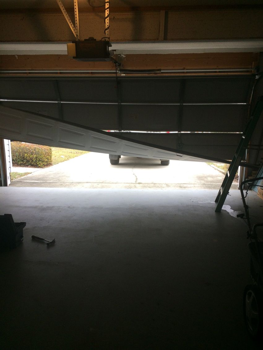 Partially closed garage door with daylight streaming in, viewed from inside a dim garage.