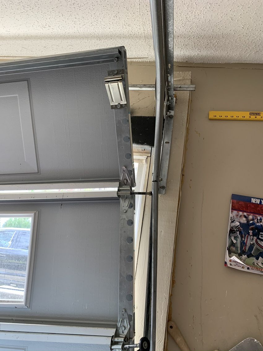Damaged garage door with bent frame and broken track beside a beige wall and hanging poster