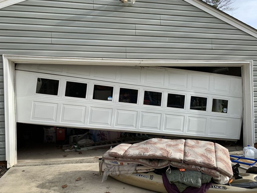 Bent white garage door bent outward, with a covered item blocking the damaged doorway.