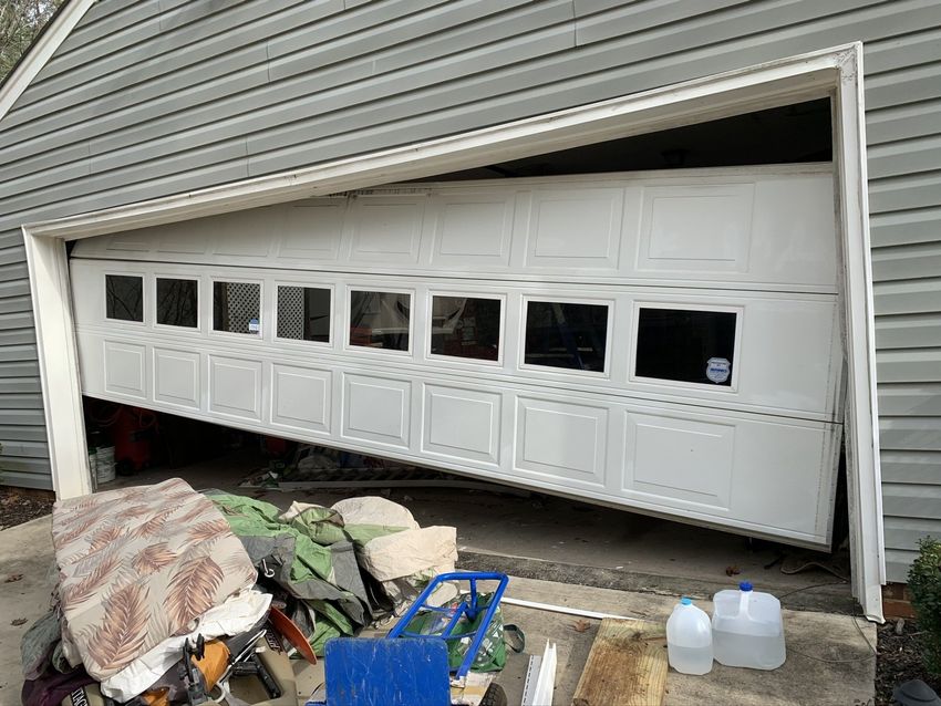 Damaged garage door bent outward, with debris piled in front of the opening.