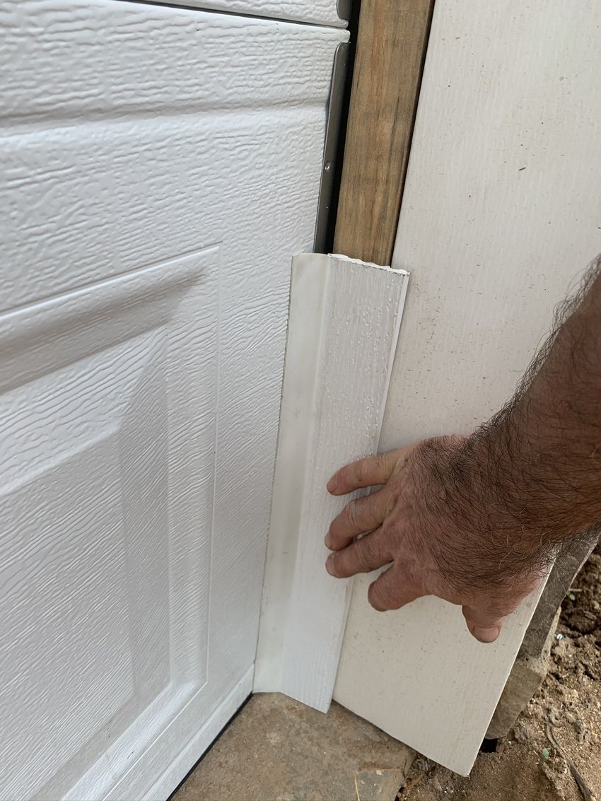 Hand placing a white trim board at the base of a garage door corner
