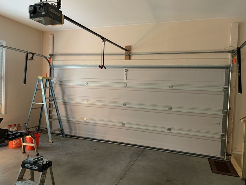 Garage interior with a white sectional door, ladder, and garage door opener rail mounted overhead