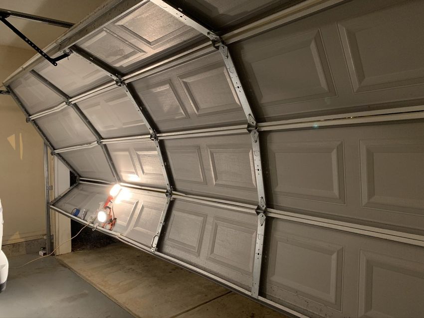 Open garage door with white paneled sections and a light glowing inside.