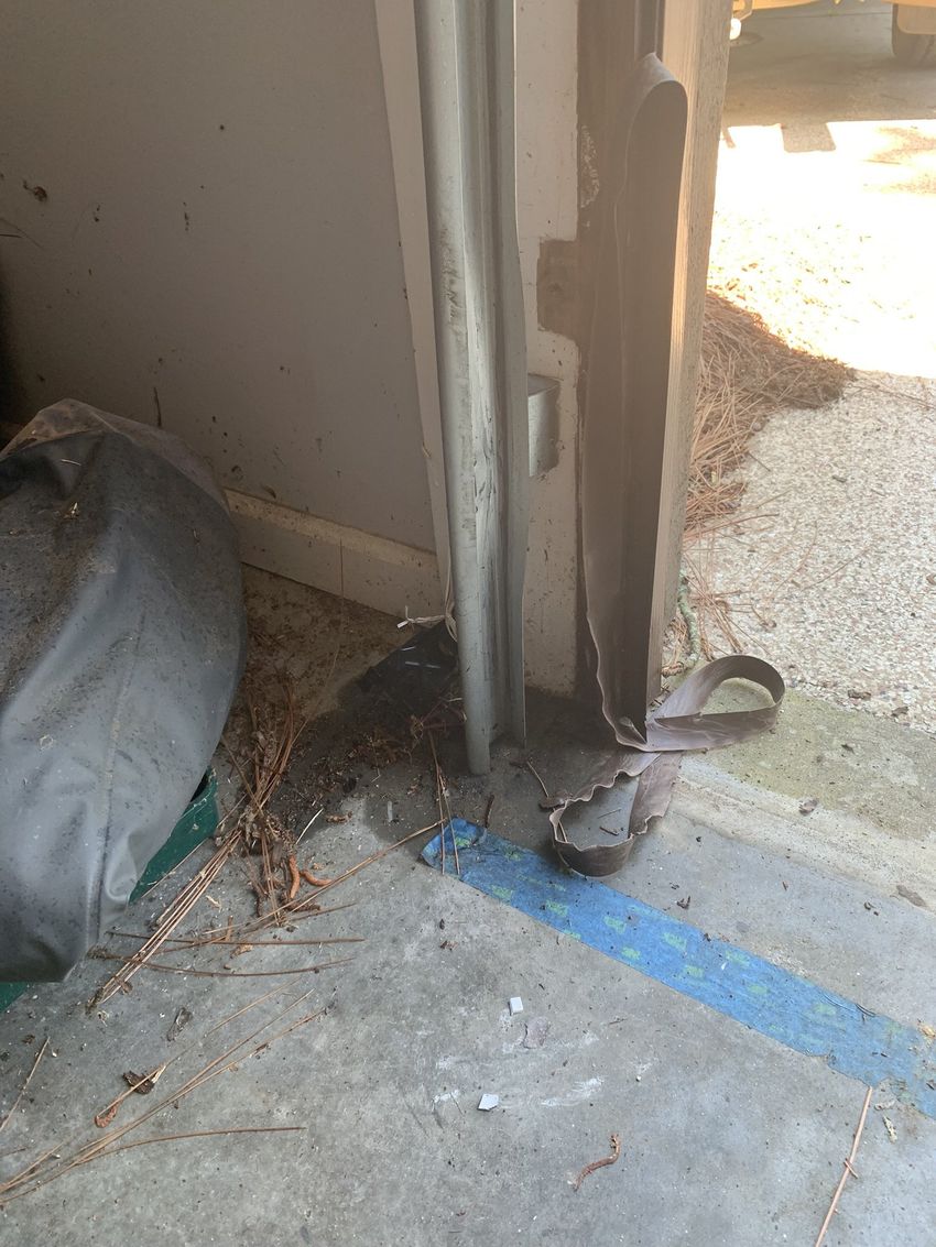 Damaged doorway with peeling frame, blue tape on the floor, and debris near the threshold