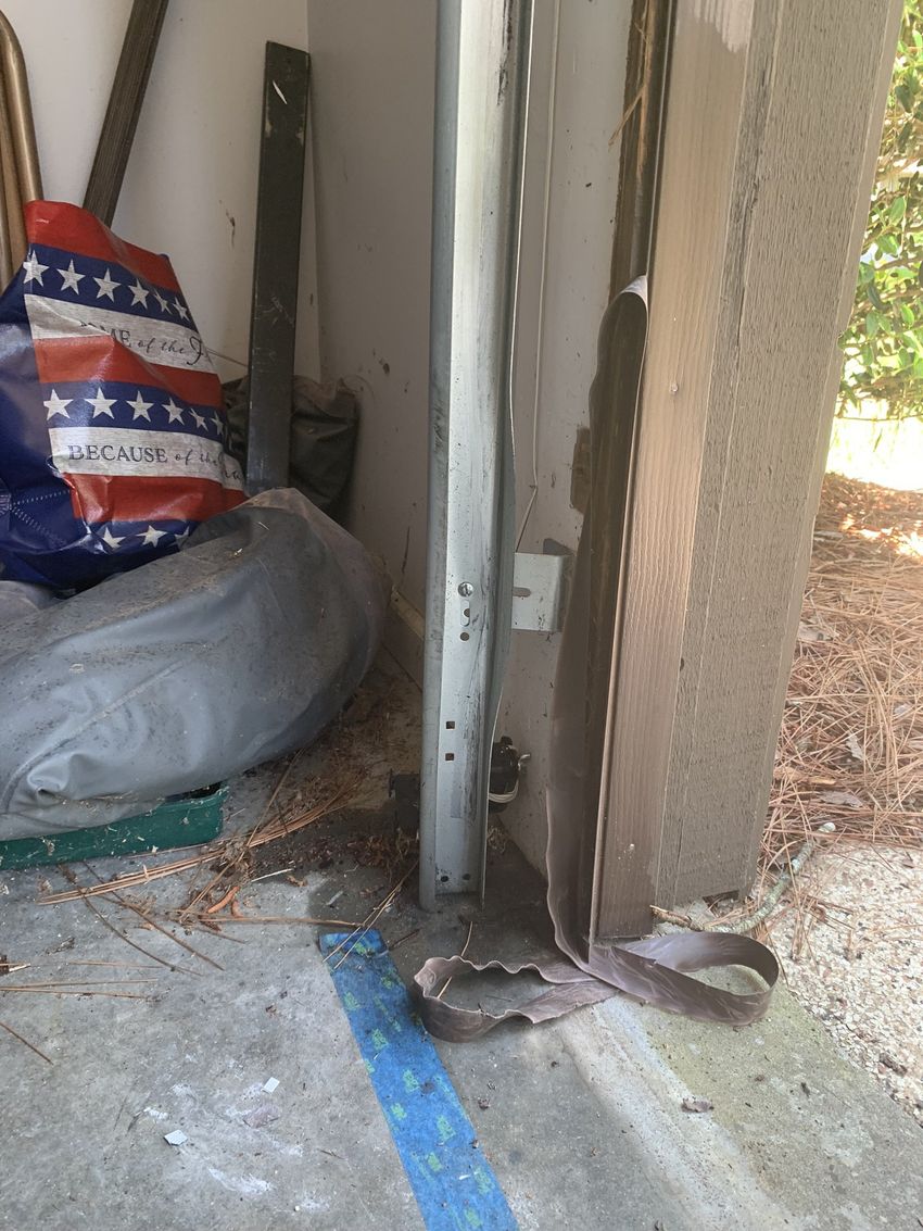 Bent metal post beside a doorway, with a bag and broom in a cluttered garage corner.