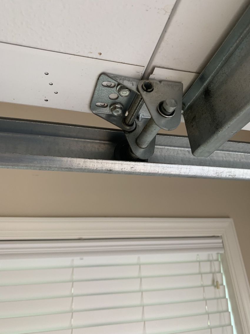 Close-up of a metal window hinge bracket above white blinds and a gray window frame