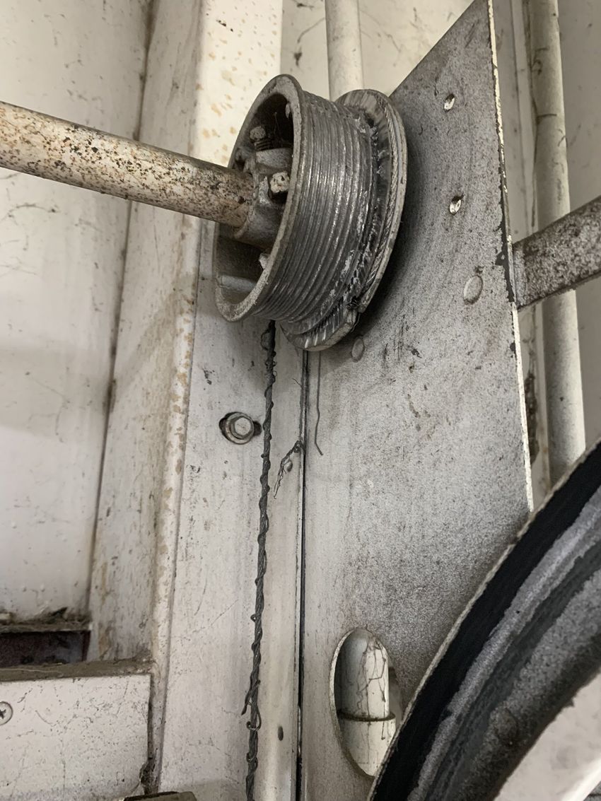 Close-up of a damaged cable spool mounted on a dirty white metal wall.