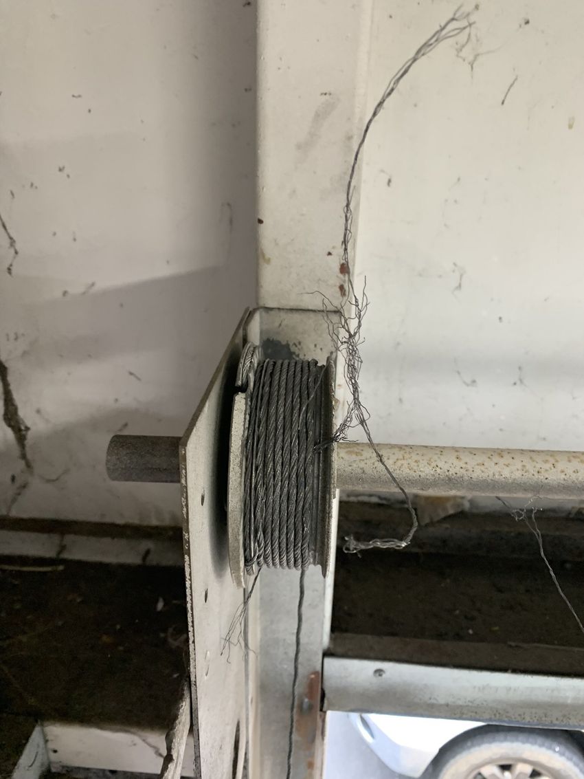 Frayed cable spool mounted on a white wall near a doorway, with exposed wires hanging down