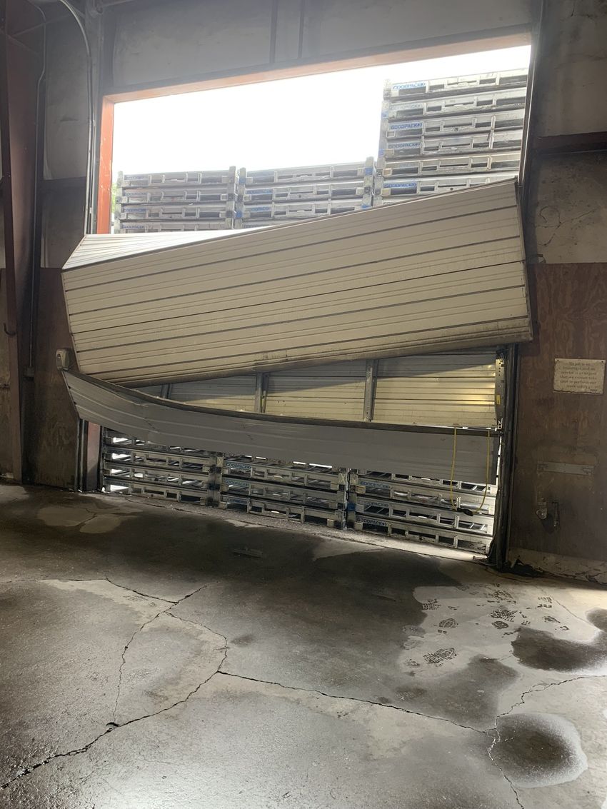 Bent warehouse door bent outward, with stacked pallets visible behind it