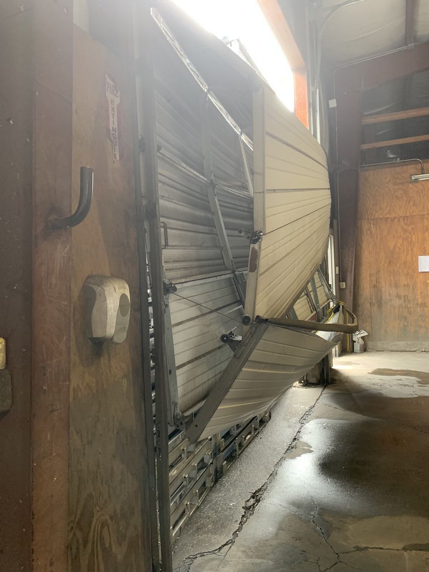Collapsed metal shutter blocking a narrow alley, with water on the ground and damaged panels leaning outward