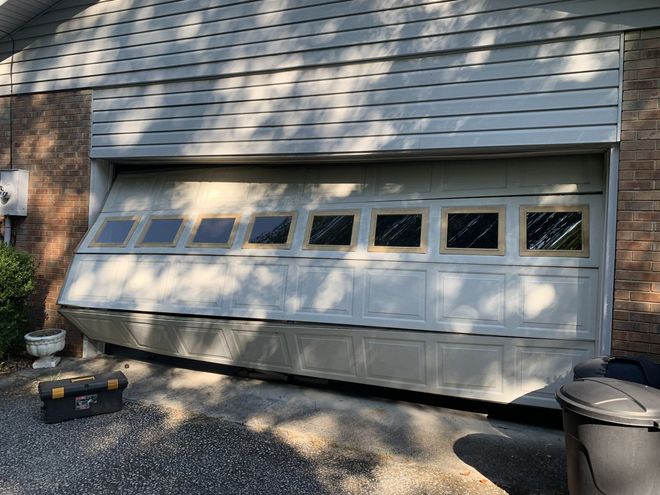 Residential garage with a white paneled door, brick trim, and sunlight casting shadows across the siding.