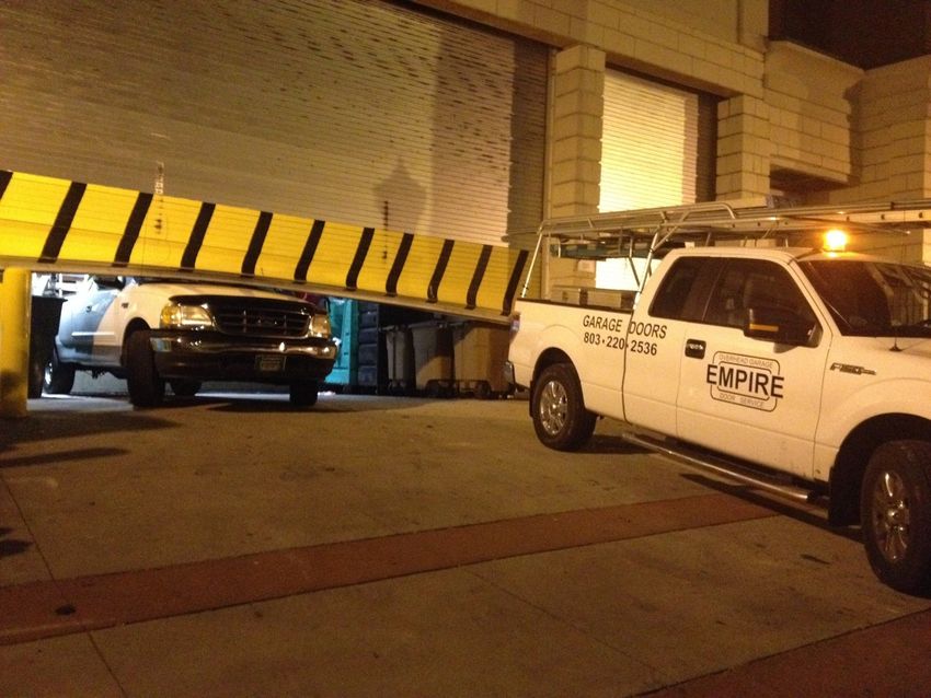 Tow truck lifting yellow-black striped barrier at a parking garage entrance, with a white pickup nearby.