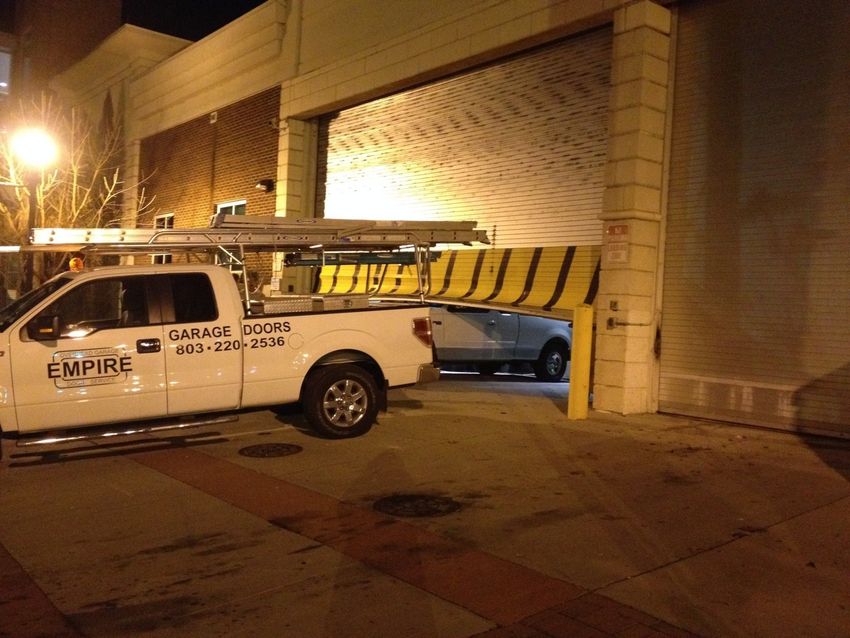 Tow truck wedged under low garage door at night, with a yellow-and-black barrier across the opening.
