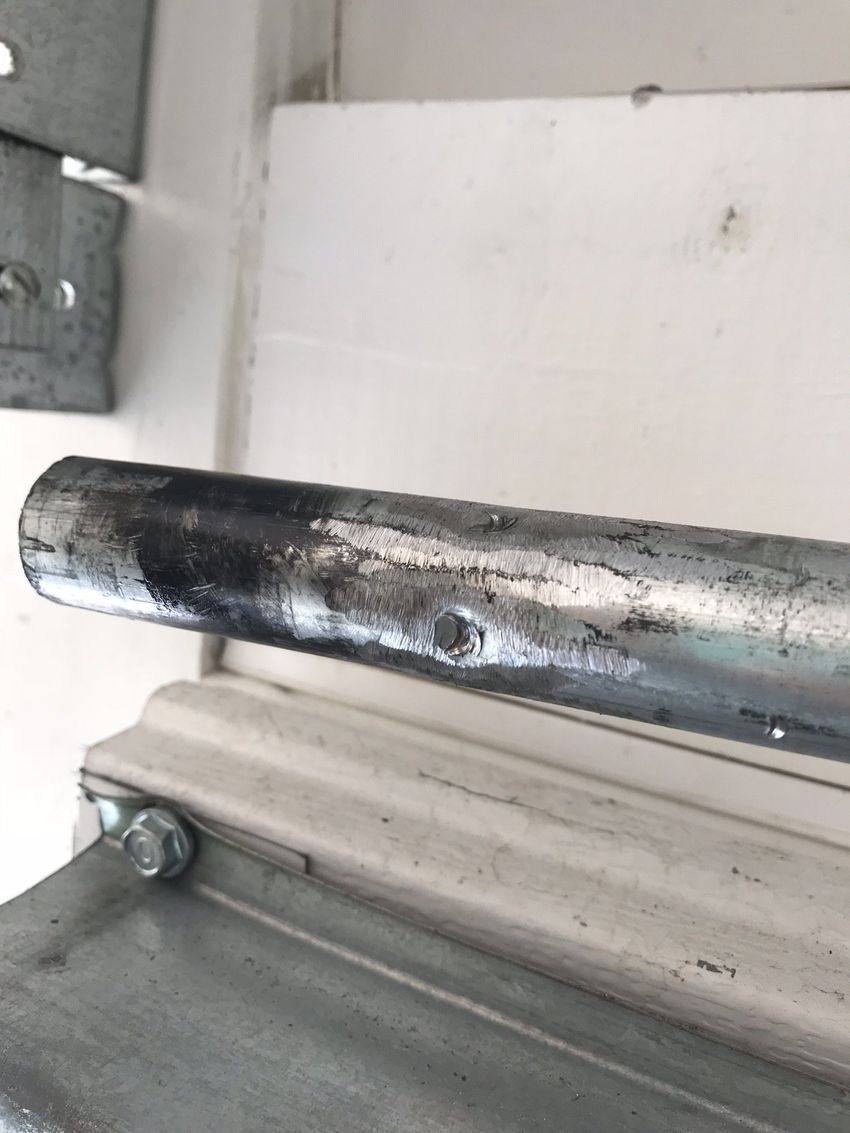 Close-up of a worn black metal pipe attached to a light gray wall bracket.