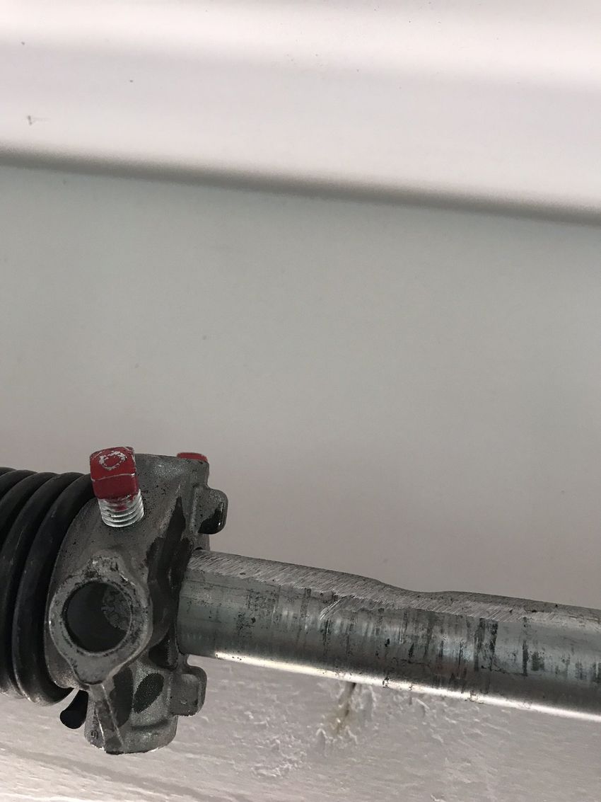 Close-up of a metal rod end with a black rubber boot and small red cap on a light wall background